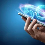 A digital illustration of a 5G logo between a human and robotic hand, set against a blue glowing city and network grid, representing Pakistan’s move toward 5G services.